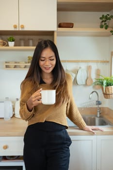 Smiling pretty woman enjoying a cup of coffee while sitting on kitchen counter.