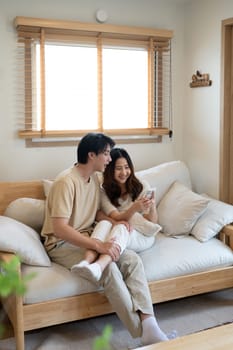 Relaxed asian couple watching online content on a smart phone in the living room.