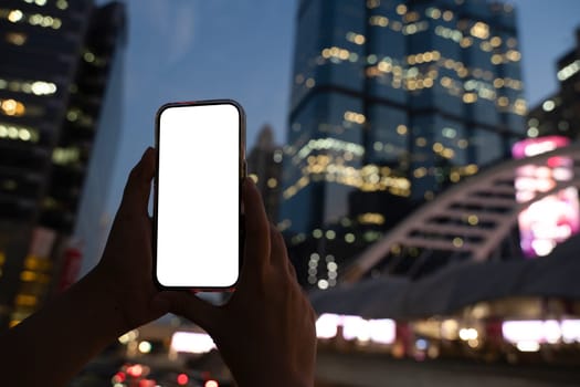 Hands holding smartphone with urban skyscrapers at night in the background.
