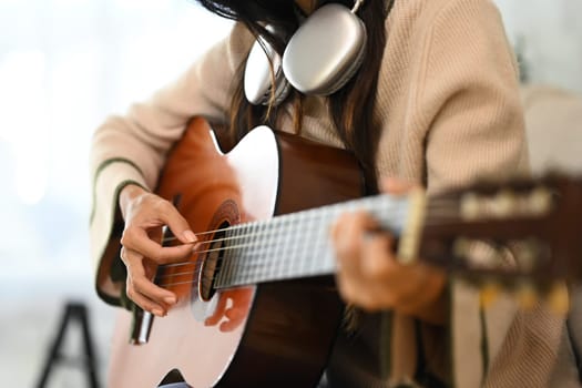 Close up of woman playing acoustic guitar with headphones around neck.
