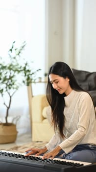 Young beautiful woman playing electric piano in living room.
