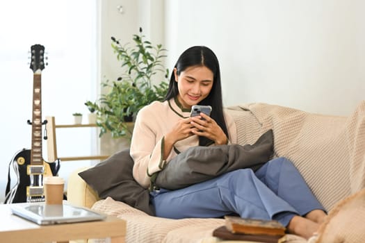 Smiling young beautiful woman relaxing and using mobile phone on sofa.