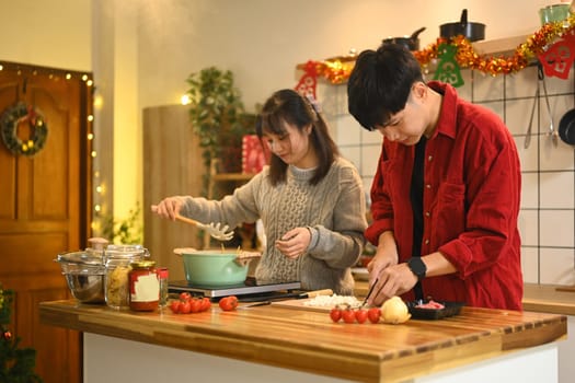 Happy young couple enjoying a cozy holiday cooking together in kitchen decorated with Christmas ornaments.