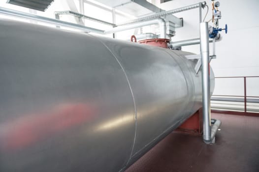 Outdoor Atmospheric Pressure deaerator. Close-up of a large metallic tank in an industrial facility, featuring pipes and equipment.