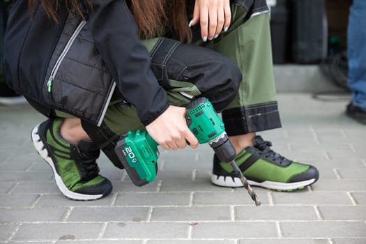 A woman confidently shows her DIY skills with a green electric drill, highlighting her stylish workwear