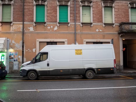 Cremona, Lombardy, Italy October 15th 2024 White delivery van parked on a city street with an old, weathered building in the background
