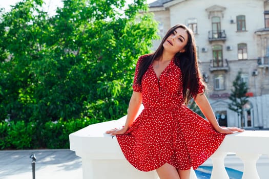 Beautiful woman in a red summer dress walking through the streets of the city