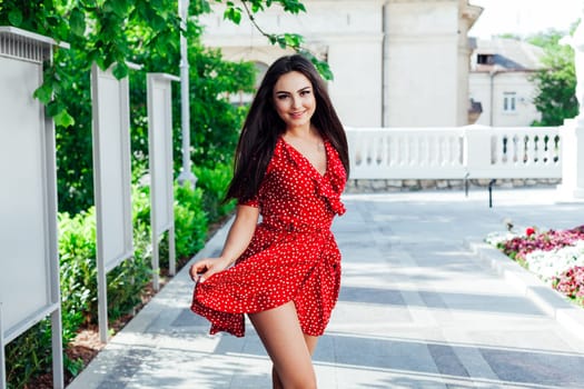 Beautiful woman in a red summer dress walking through the streets of the city