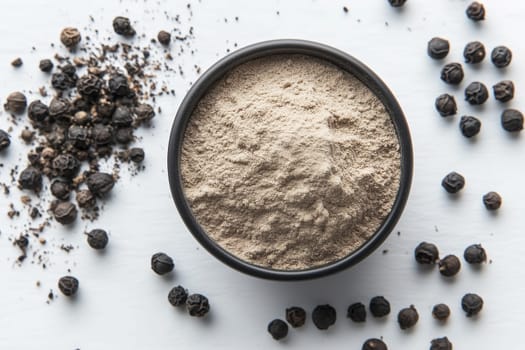 A bowl of finely ground black pepper sits on a white surface, surrounded by whole peppercorns. This arrangement showcases the spice's versatility in cooking.