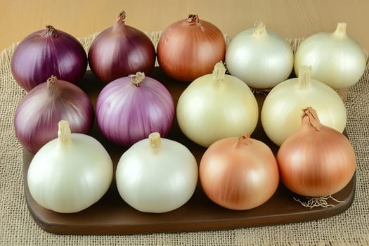 Various colorful onions are arranged neatly on a wooden tray. The display includes red, white, and yellow onions, highlighting their shapes and colors.