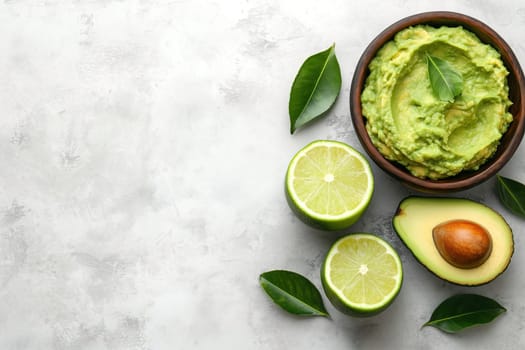 Guacamole is served in a rustic bowl alongside halved limes and a whole avocado. Green leaves add a fresh, vibrant touch to the arrangement on a neutral gray backdrop.