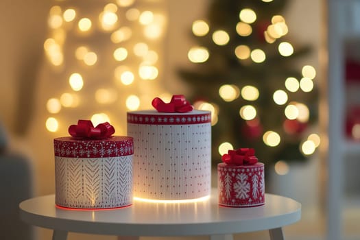 Beautifully wrapped gift boxes in red and white sit on a table, surrounded by a warm holiday ambiance created by twinkling lights.