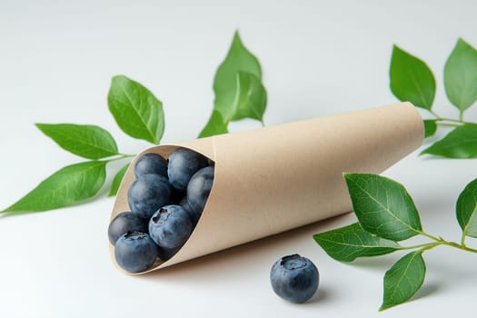 A paper cone filled with freshly picked blueberries rests on a light backdrop, complemented by vibrant green leaves, highlighting healthy snacking options.