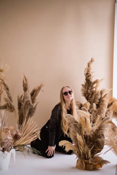 A woman photographer, a blonde with a camera, seriously with sunglasses in the production studio. Wearing a black clothes on a brown background