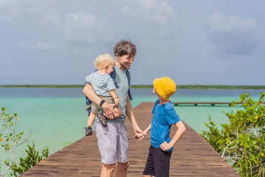 Father with his toddler and teenage sons exploring wooden pier over the turquoise waters of Bacalar Lake, Mexico. Peaceful tropical travel destination concept.