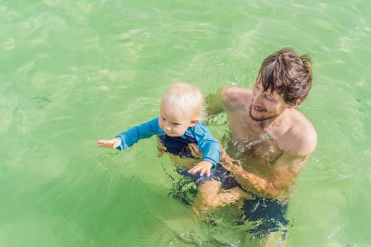Father with his toddler son swimming in the turquoise waters of Lake Bacalar. Family bonding, summer vacation, and outdoor fun in Quintana Roo, Mexico concept.