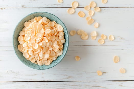 A turquoise bowl holds a generous portion of crunchy cornflakes on a rustic wooden table. Some flakes are scattered around, adding to the kitchen atmosphere.