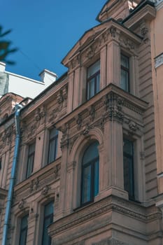 Close-up of a historic building's ornate facade, showcasing classical architectural details, including arched windows and decorative stonework under a clear blue sky