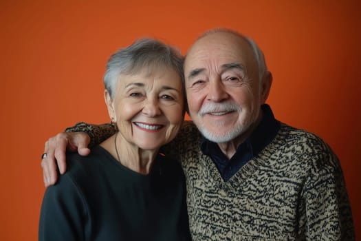An elderly couple stands close, smiling warmly at the camera with their arms around each other.