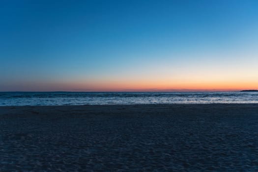 Serene beach scene at sunset with gentle waves and a calm horizon, creating a peaceful atmosphere with soft twilight colors reflecting on the wate