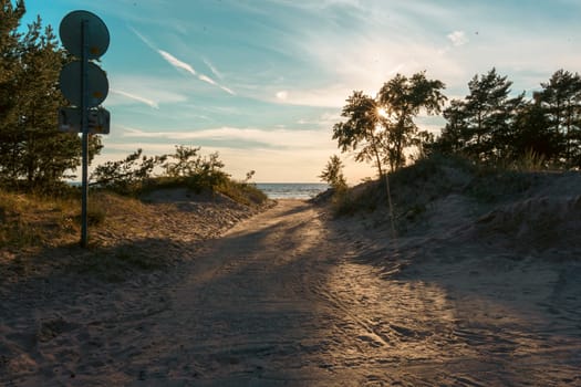 A sandy path winds through coastal dunes, leading to the beach under the warm glow of a setting sun, creating a tranquil and scenic approach to the shoreline