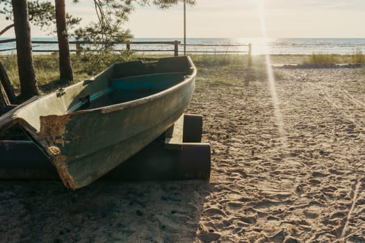 An old boat rests on a sandy beach as the sun sets over the water, casting warm rays and creating a peaceful and serene atmosphere in a rustic coastal scene