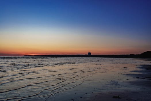Serene beach scene at sunset with gentle waves and a calm horizon, creating a peaceful atmosphere with soft twilight colors reflecting on the wate