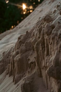 A close-up view of a textured sand formation on a dune, illuminated by warm sunset light, capturing natural patterns and the serene beauty of coastal erosion in a peaceful setting
