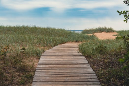 A wooden boardwalk winds through grassy dunes, leading toward the beach under an overcast sky, capturing the serene and rustic beauty of a coastal landscape