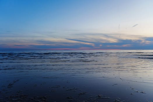 A peaceful sunset over a calm ocean with gentle waves and a colorful sky, creating a tranquil and scenic landscape. The image captures the beauty of twilight with no people in view.
