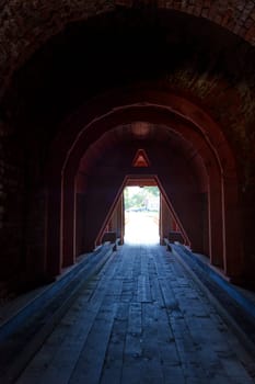 Interior view of a dark, arched passageway in an ancient stone structure, leading toward an opening filled with daylight. The scene captures a mysterious and historic atmosphere