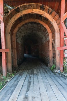 An arched entrance leading into a dark tunnel constructed with wood and stone inside a historic fortress. The dim passageway evokes a sense of mystery and medieval architecture