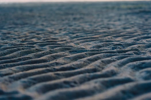 A close-up of rippled sand patterns on a beach at low tide, capturing natural textures and wavy details in a tranquil coastal scene
