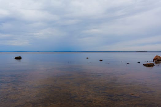 A tranquil seascape with calm water and scattered rocks beneath a cloudy sky, capturing the peaceful and minimalist beauty of nature along the horizon