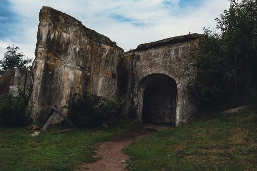 An abandoned stone fortress with weathered walls and an arched entrance, set in a grassy area, evoking a sense of history and decay in a quiet, rural setting