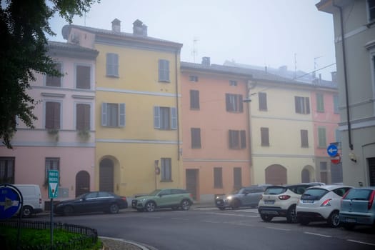 Cremona, Lombardy, Italy - November 7th 2024 Pastel-colored buildings line a street with parked cars on a foggy morning in a quiet italian town