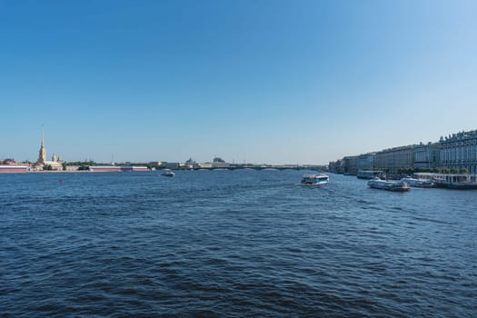 Scenic view of a wide river with a historic bridge spanning across, framed by urban buildings under a clear blue sky. Peaceful waterfront scene with gentle waves