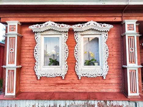 A beautifully detailed wooden house features ornate white carvings around two flower-filled windows against a coral-painted exterior.