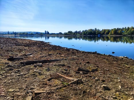 A serene lake stretches out beneath a blue sky with scattered clouds, framed by a grassy hillside.