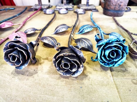 Colorful metal roses crafted by artisans are displayed beautifully on a table at a local market under bright sunlight.