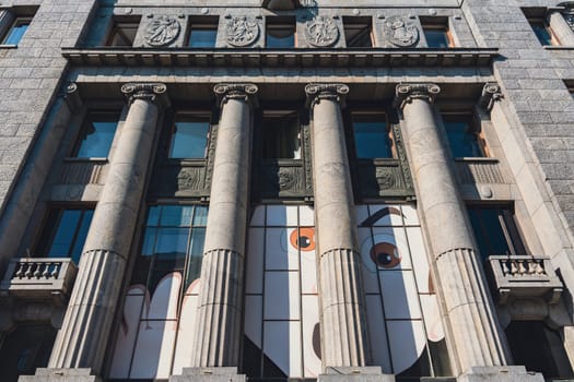Close-up of a historic building's facade with grand columns, featuring a striking modern mural on the windows. Classical and contemporary elements create a unique visual contrast