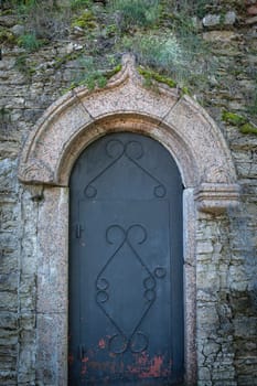 An ancient stone door with an arched opening and forged elements. Rustic architecture surrounded by moss and textured masonry creates an atmosphere of abandonment and history