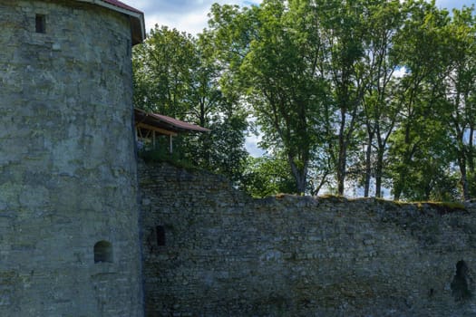 A medieval stone fortress with a tall round tower and extensive walls, set against a clear blue sky. The structure stands on a grassy area, evoking historical significance and rustic charm