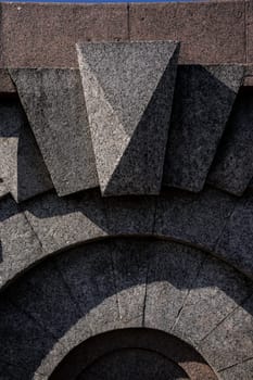 Detailed view of a granite structure featuring bold geometric shapes, including triangular and arched elements, showcasing texture and craftsmanship under natural light
