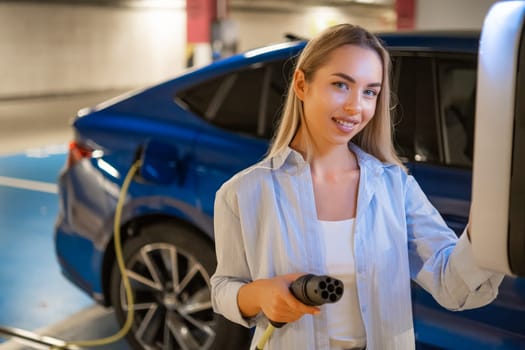 Portrait of blonde woman charging her electric car at a parking station in a well lit garage.