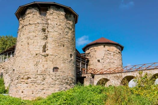 Close-up view of ancient stone fortress towers connected by a bridge and featuring arched entrances, set against a clear blue sky. Historic architecture and medieval charm