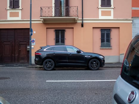 Cremona, Lombardy, Italy October 15th 2024 A black jaguar f pace is parked on a narrow street in front of a typical italian building with an orange facade