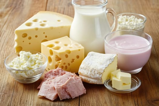 An assortment of dairy foods including cheese, milk, yogurt, and ham neatly arranged on a wooden table, ideal for nutritious recipe ideas.