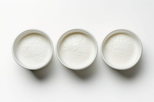Three small white bowls are placed side by side, each containing a smooth, creamy substance. The minimalist arrangement focuses on texture and color in a well-lit setting.
