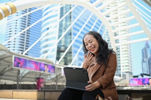 Delighted senior businesswoman using digital tablet in modern city.